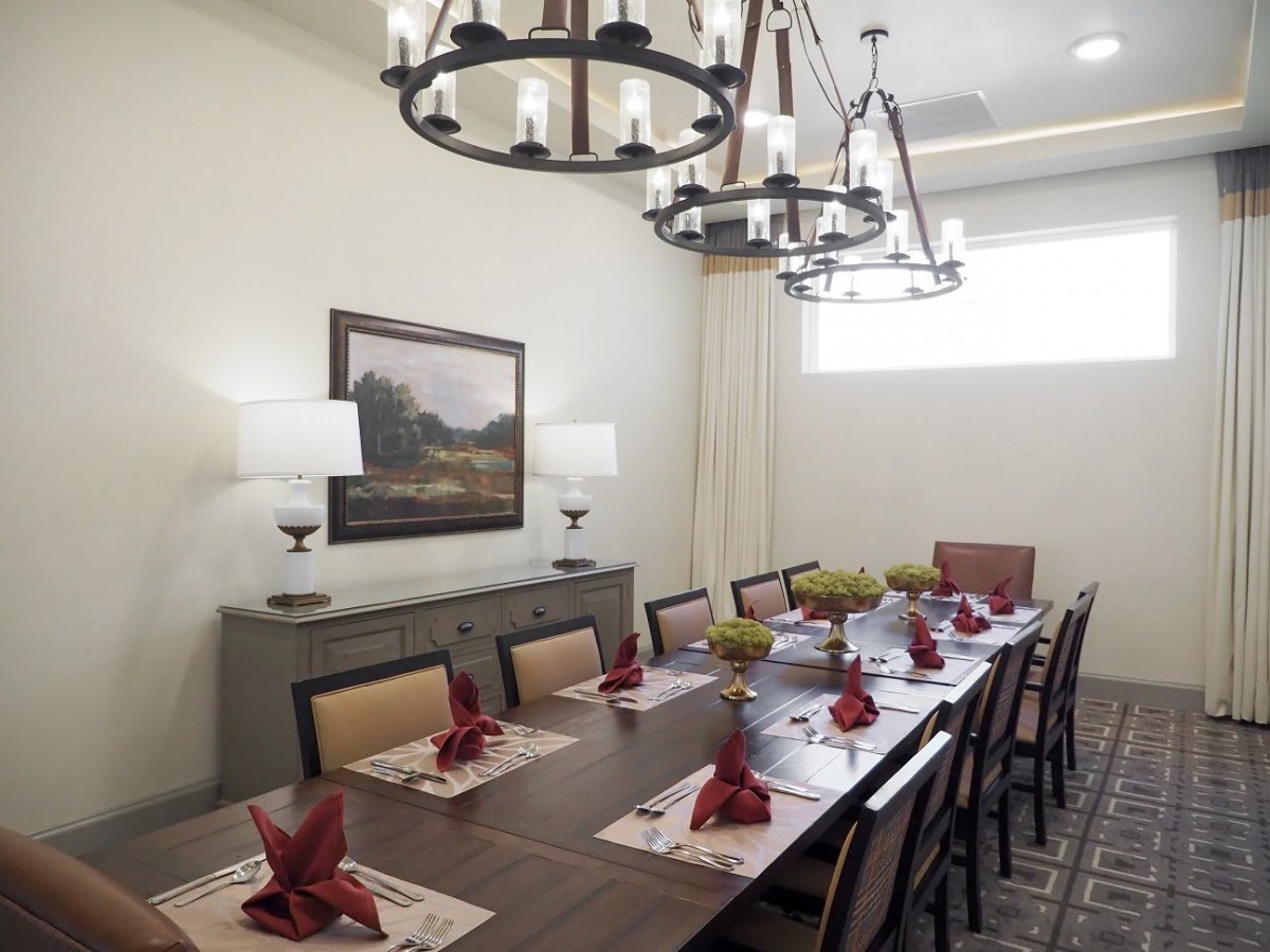 A well-decorated dining room featuring a long table with red napkins, chandeliers, and wall art.