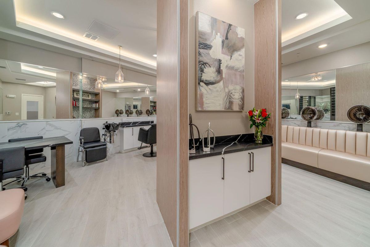 A modern salon interior featuring sleek chairs, mirrors, a sink with flowers, and abstract artwork.