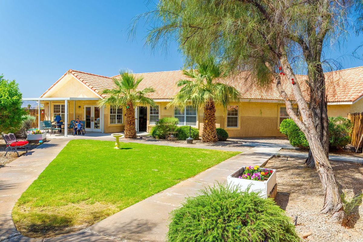 A suburban house with a lush lawn and palm trees under a clear blue sky.