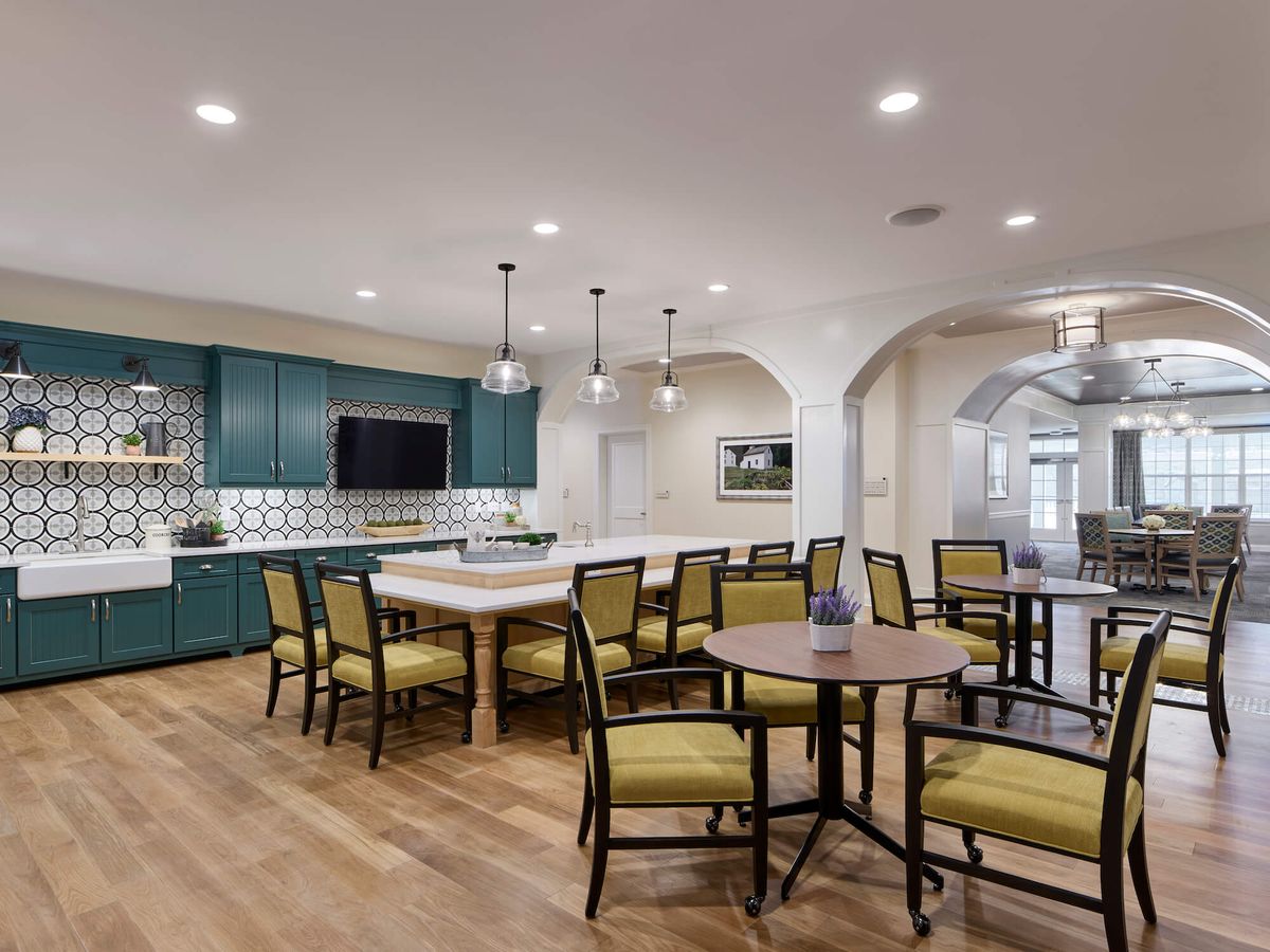 A modern open-space kitchen and dining area with teal cabinets, a large island counter, and elegant pendant lighting.