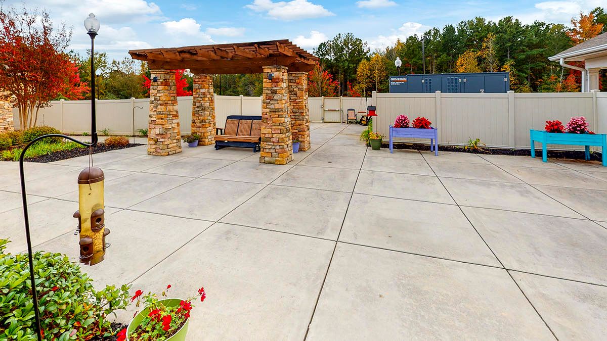 A spacious outdoor patio featuring a pavilion with stone pillars and benches, set against an autumn landscape.