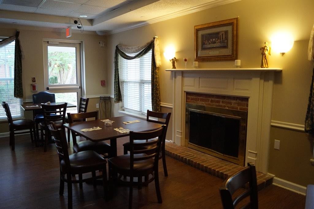 A cozy restaurant interior featuring wooden tables and chairs, a fireplace, and large windows.