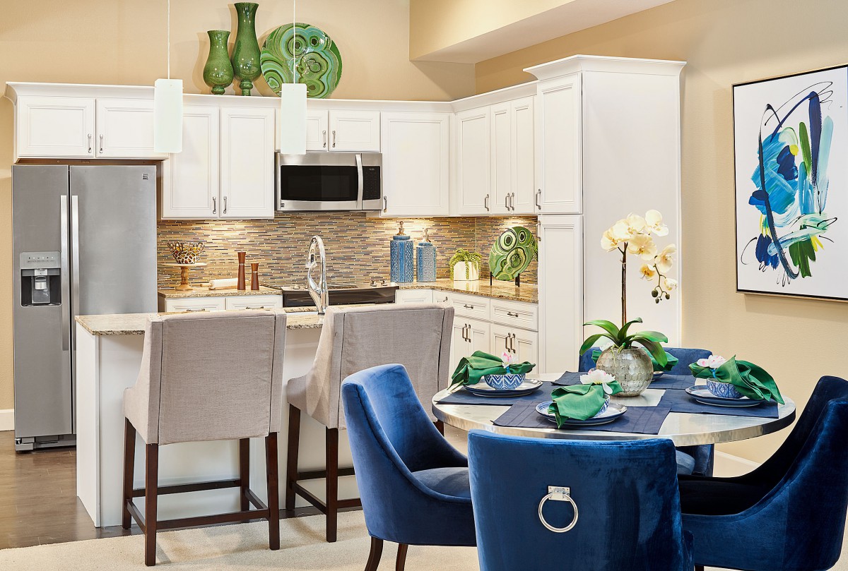 A modern kitchen and dining area featuring white cabinets, blue chairs, and a well-set table with decorative green accents.