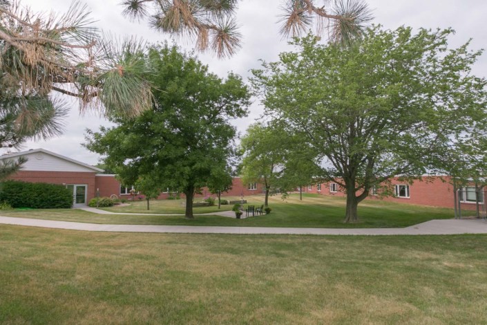 A serene outdoor park area with trees, benches, and a pathway near brick buildings.