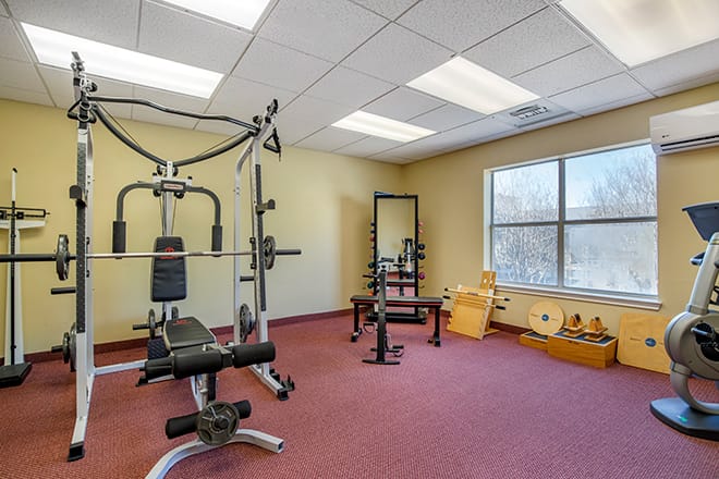 A small gym room with various fitness equipment including a weight machine and free weights.