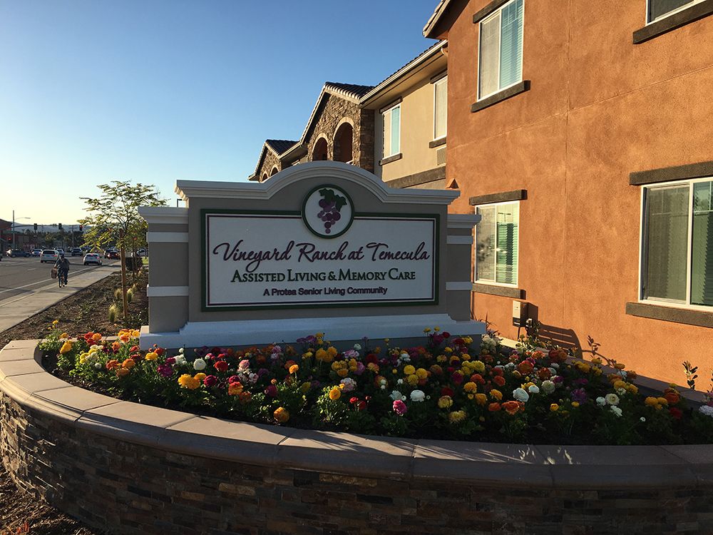 A residential sign in front of a building surrounded by colorful flowers.