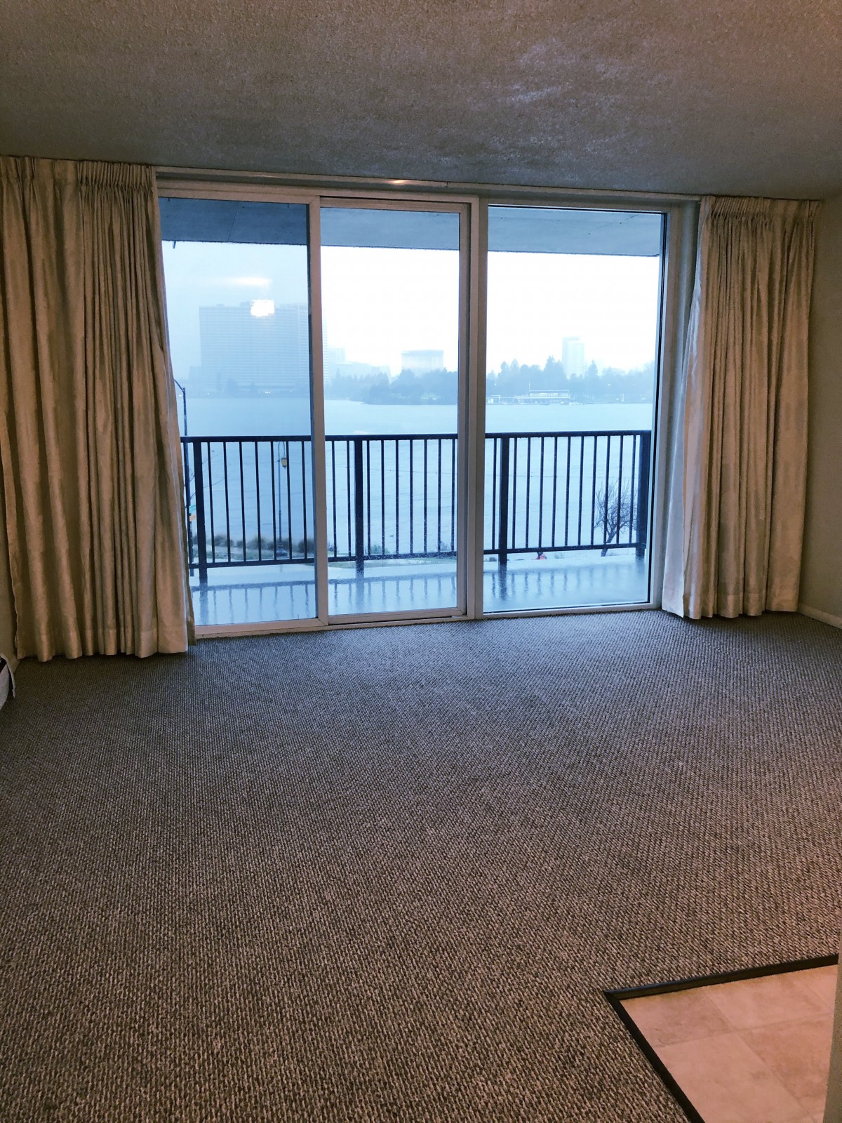 An empty room with carpet flooring, featuring large windows and a balcony view.