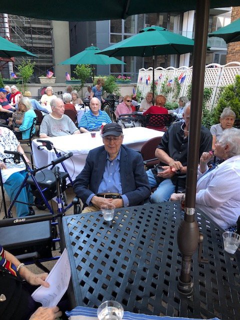 A group of people enjoying an outdoor gathering on a patio with tables and umbrellas.