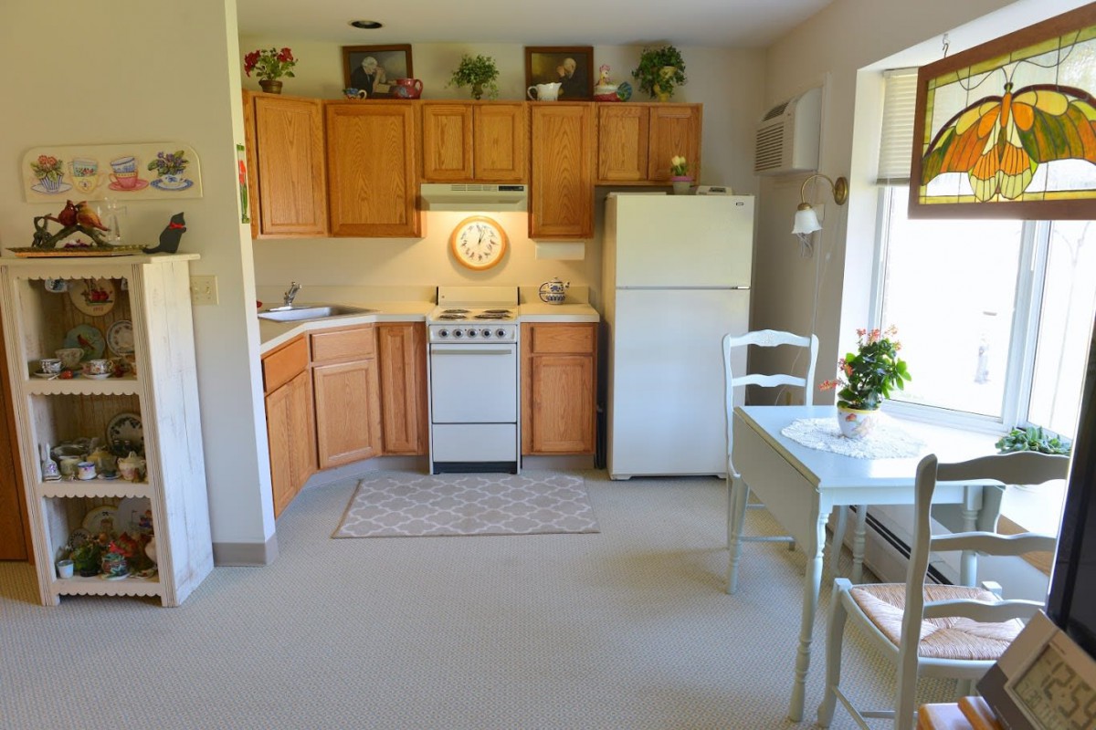 A cozy kitchen with wooden cabinets, a small stove, and a dining table by the window.