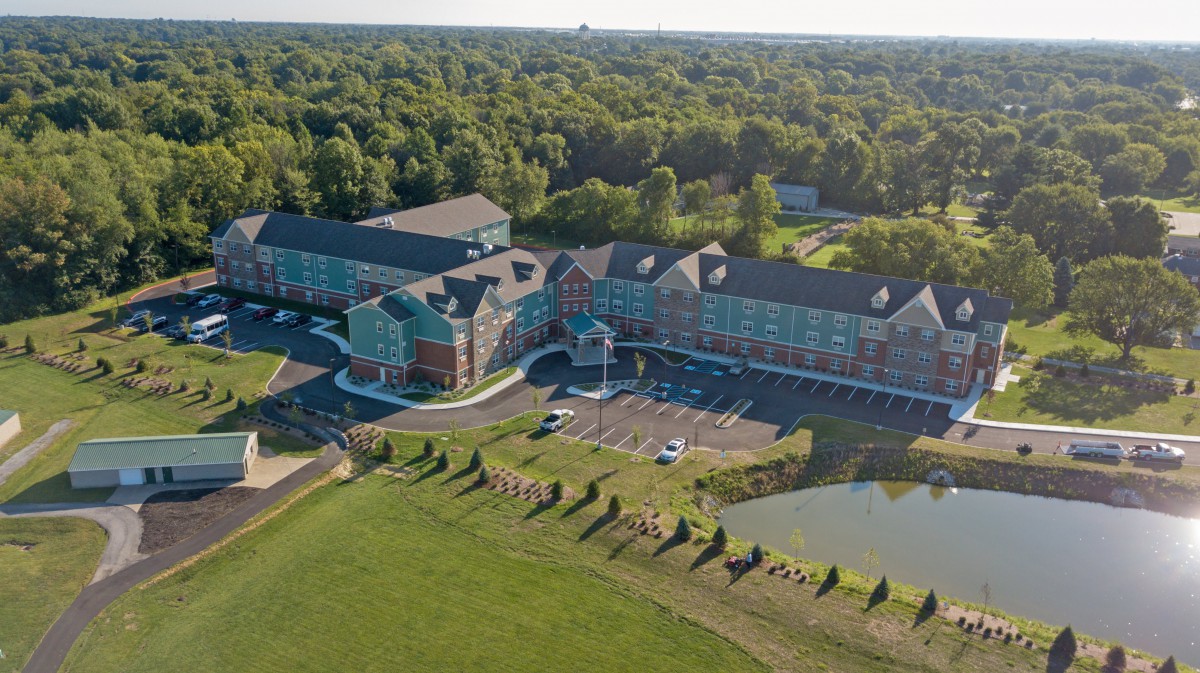 Aerial view of a large hotel complex surrounded by lush greenery and a small pond.
