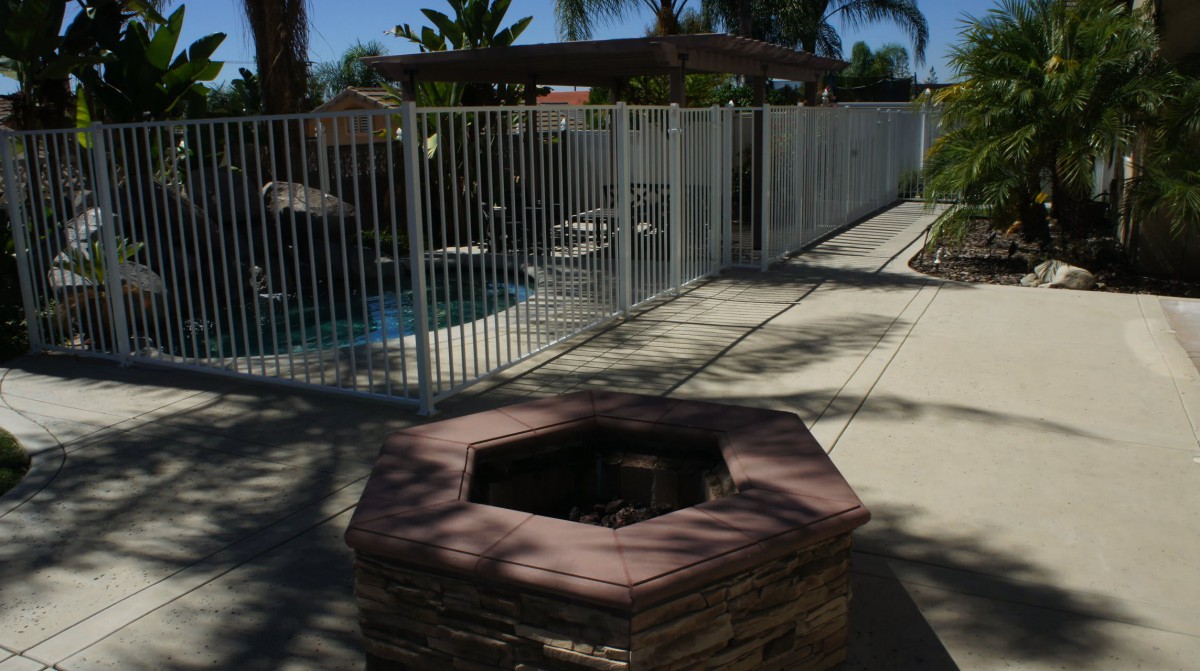 An outdoor patio area featuring a fire pit and fenced swimming pool under clear skies.