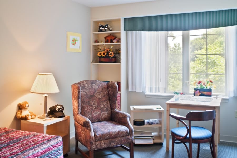 A cozy living room with a comfortable armchair, desk, and window view.