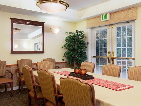 A well-lit dining or conference room with a large table surrounded by chairs, adorned with a decorative centerpiece and indoor plant.