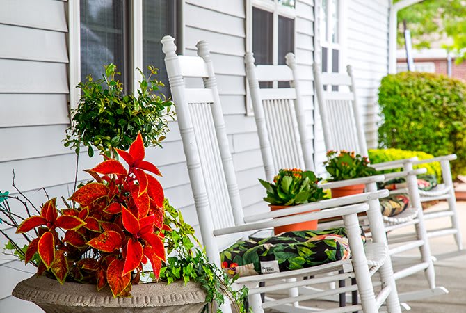 A cozy porch with white rocking chairs and colorful potted plants.