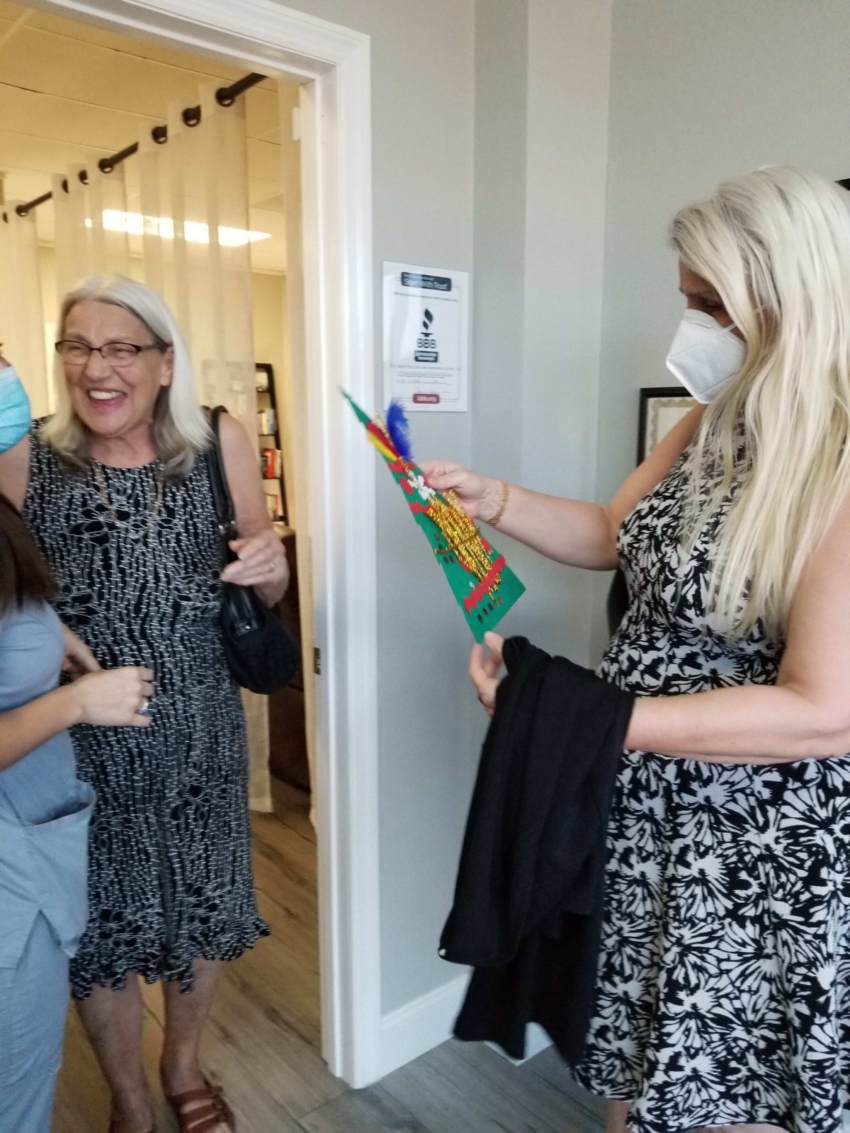 A group of women celebrating a ribbon-cutting event indoors, with one person wearing a mask.