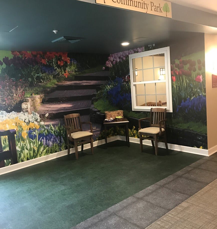 An indoor space featuring a mural of a garden scene with two chairs and a table in front of it.