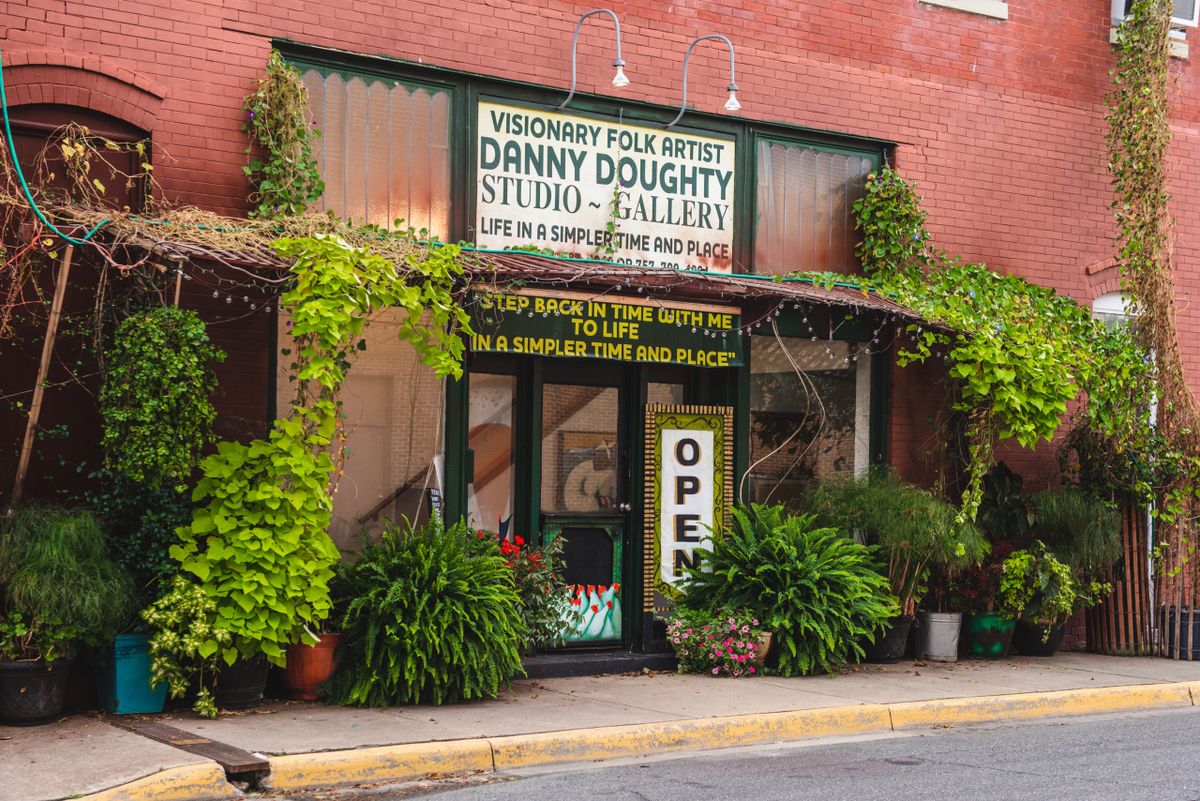 The entrance to an art gallery with greenery and a welcoming sign.