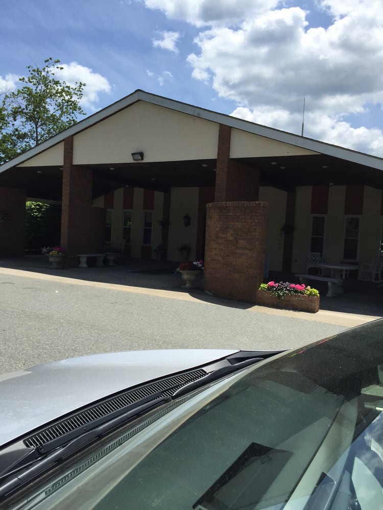 A building with a covered entryway and a parked car in the foreground on a sunny day.