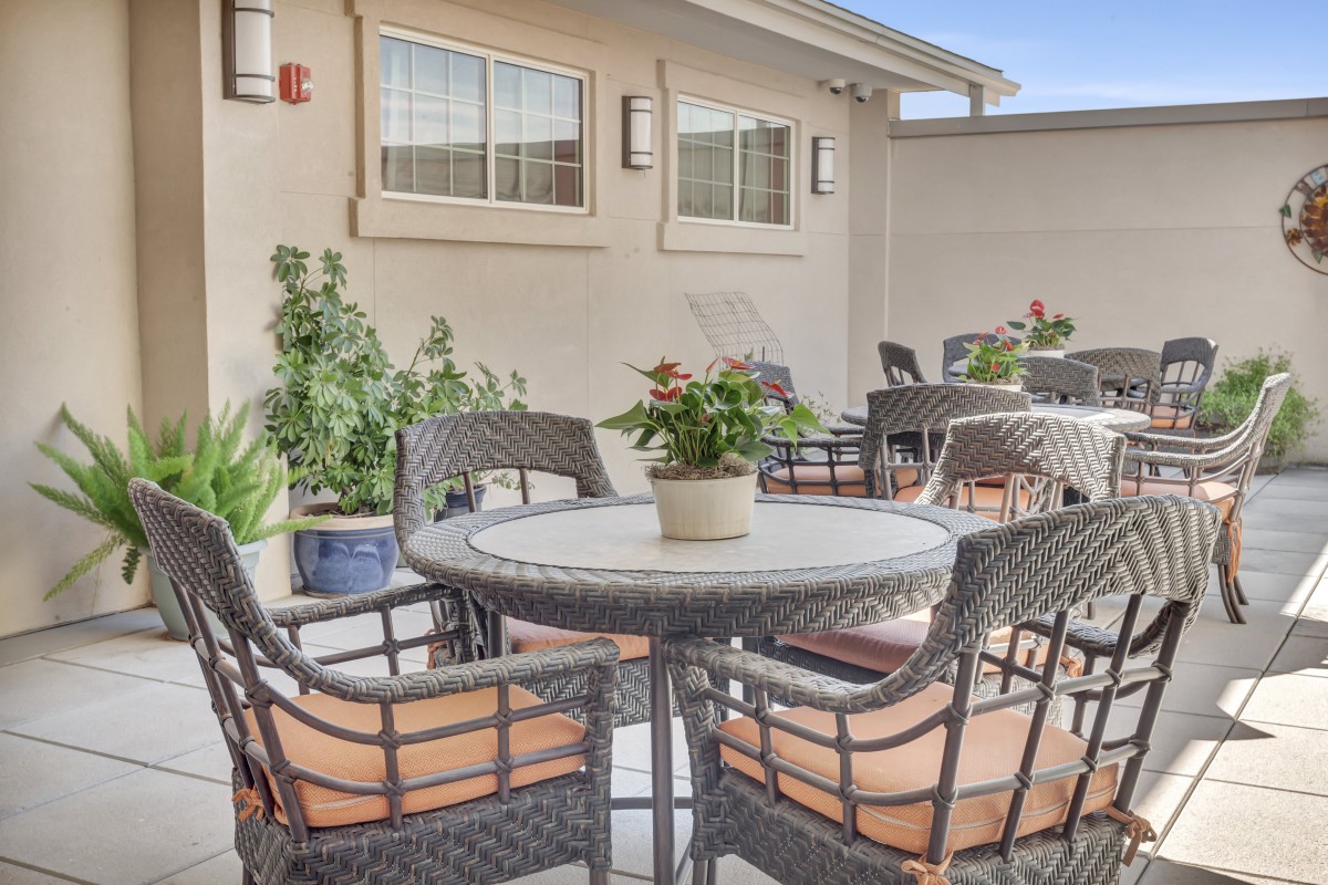 A cozy outdoor patio area with a table, chairs, and potted plants.