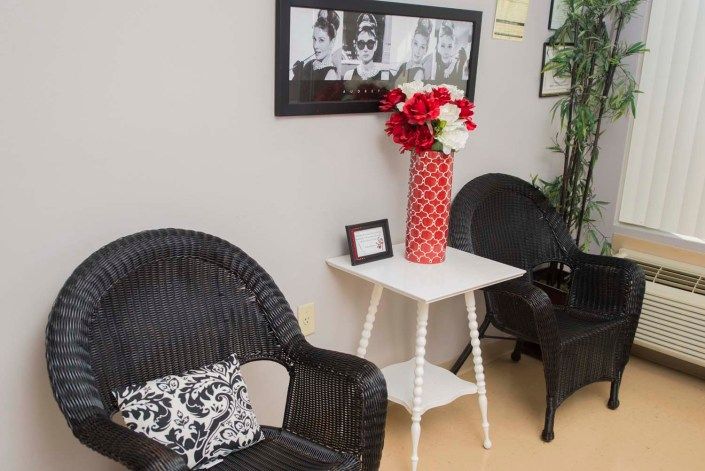 A cozy seating area with wicker chairs, a white table, and a red vase with flowers, complemented by wall art.