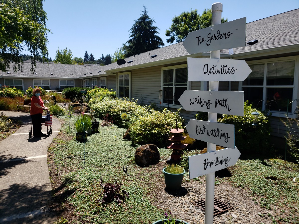 A garden scene with a signpost pointing to various activities and locations, surrounded by lush greenery.