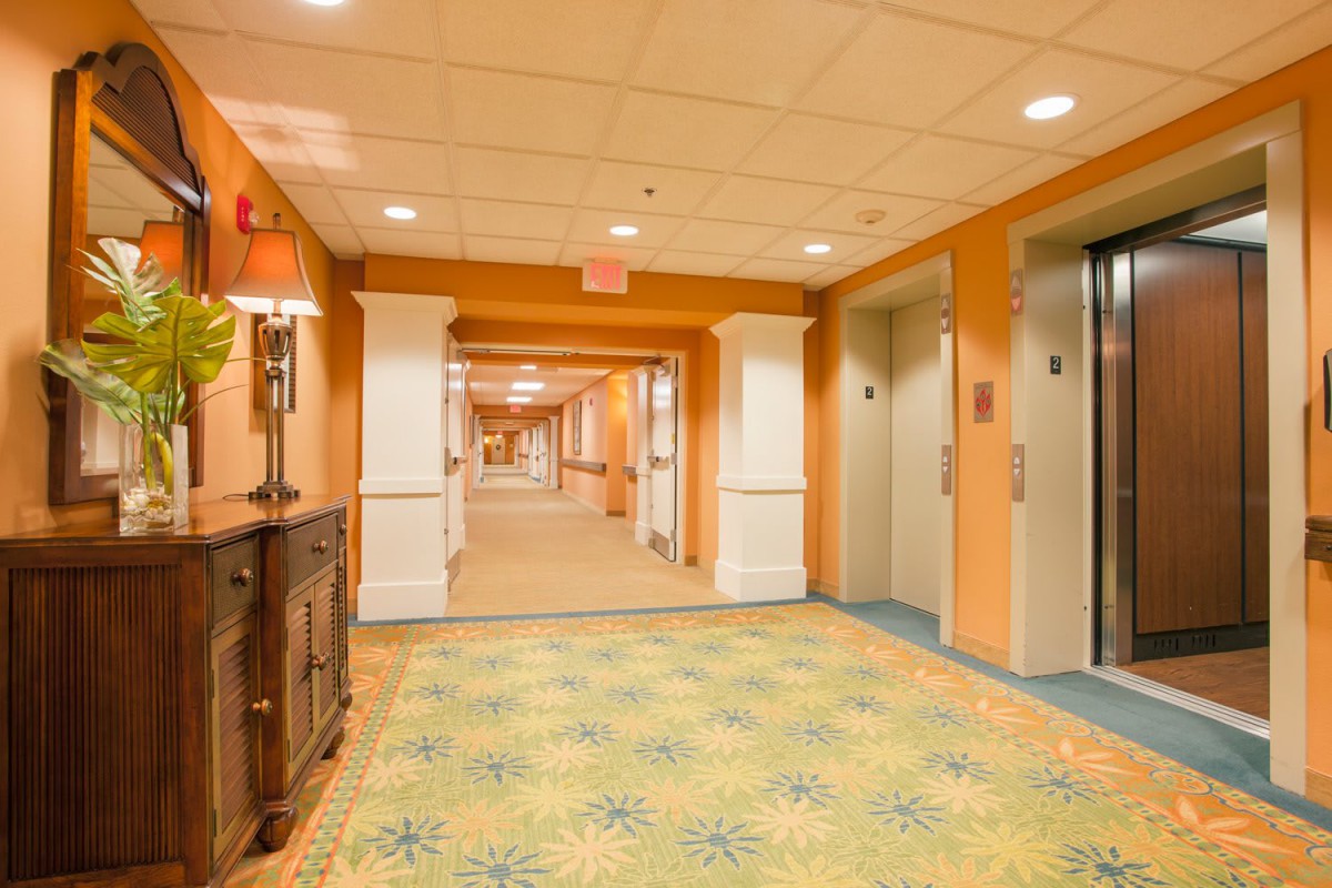 A brightly lit hotel lobby with elevators and a hallway extending into the distance.