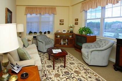 A cozy living room with traditional furnishings, featuring comfortable sofas and armchairs, a patterned carpet, and decorative curtains.