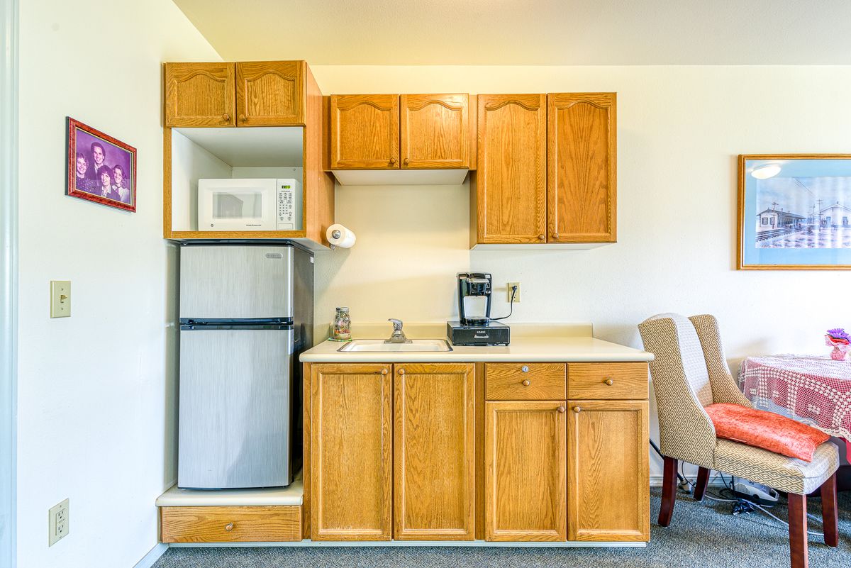 A compact kitchenette with wooden cabinets, equipped with a microwave, refrigerator, sink, and coffee maker.