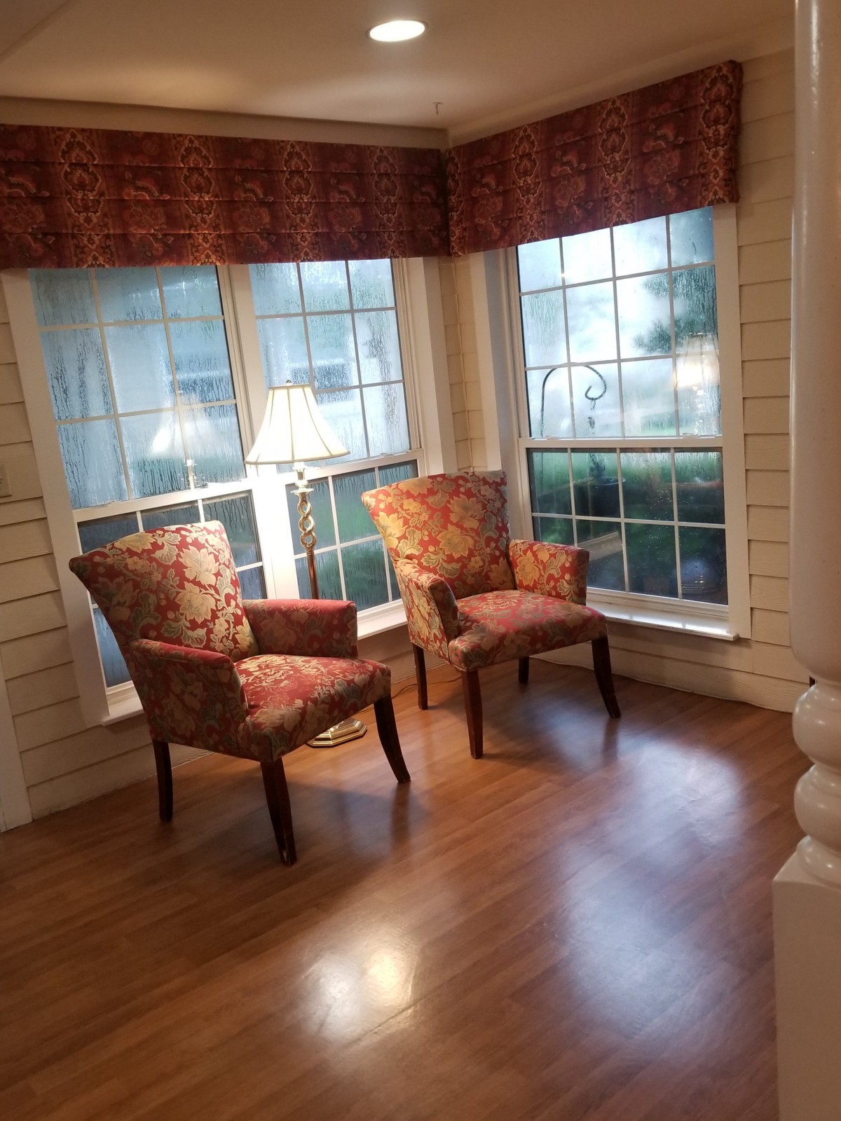 A cozy sitting area with two chairs near large windows and a lamp.