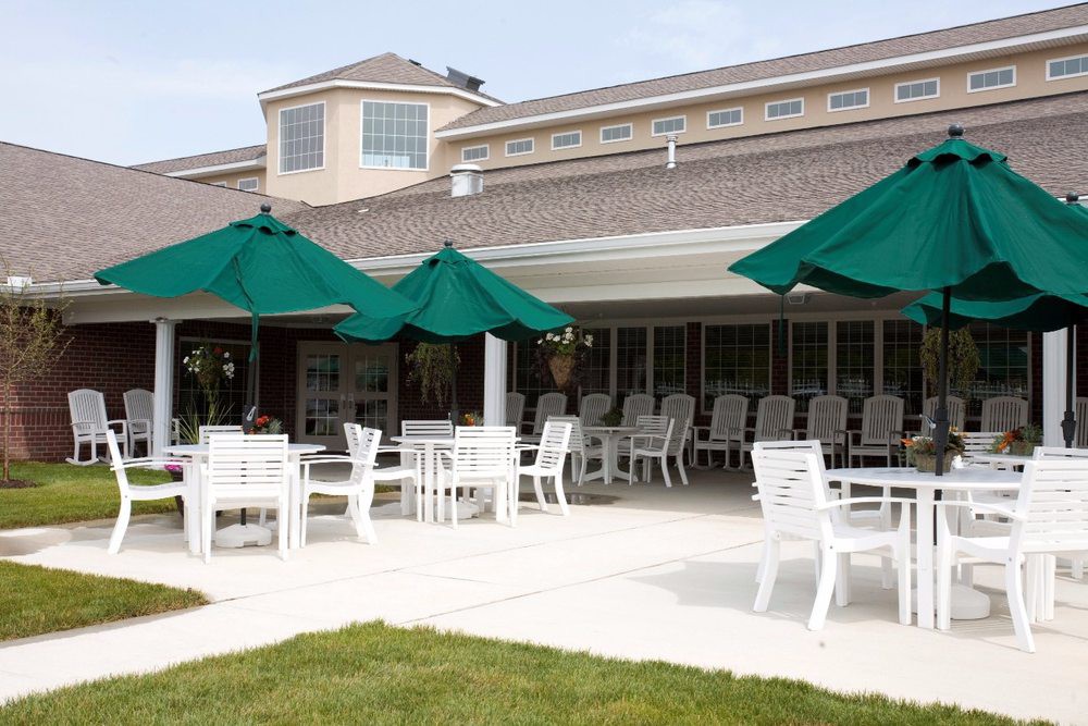 An outdoor patio area with white tables and chairs under green umbrellas.
