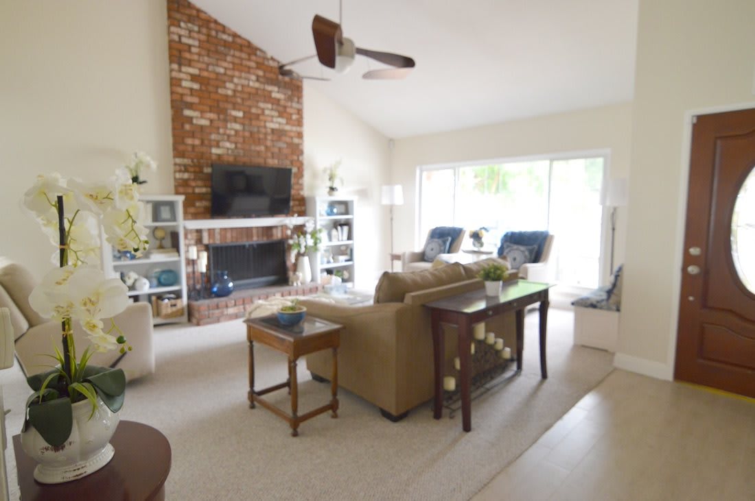 A cozy living room featuring a brick fireplace, comfortable seating, and a large window allowing natural light.