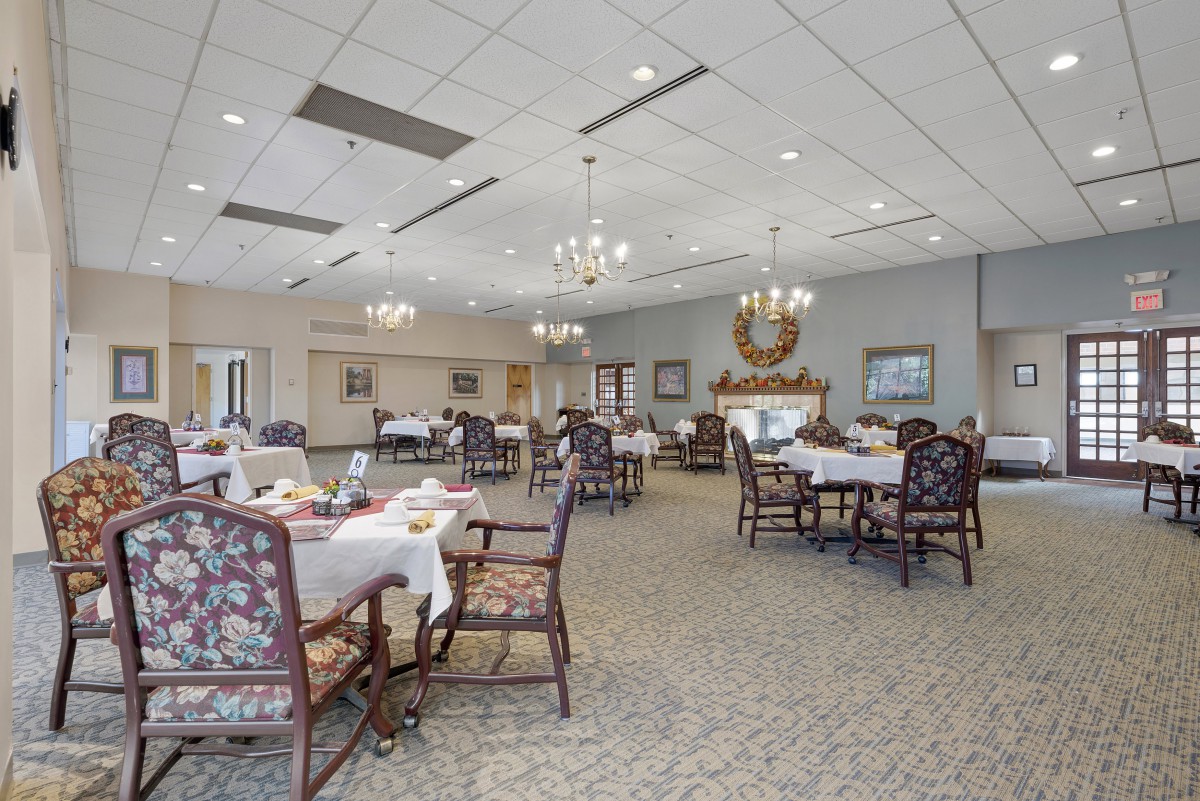 An elegant dining room with neatly arranged tables and chairs, featuring chandeliers and decorative elements.