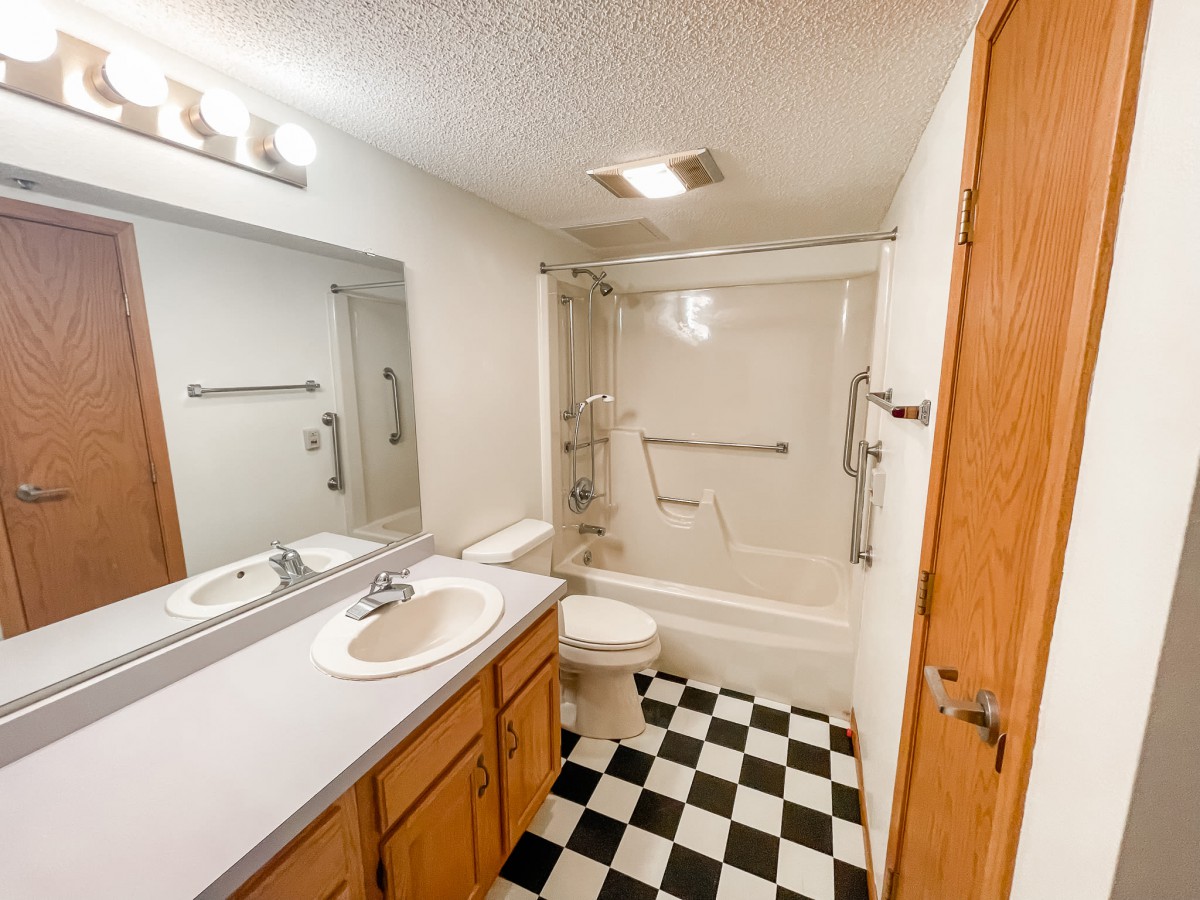 A small bathroom with a shower, sink, and checkerboard tile flooring.