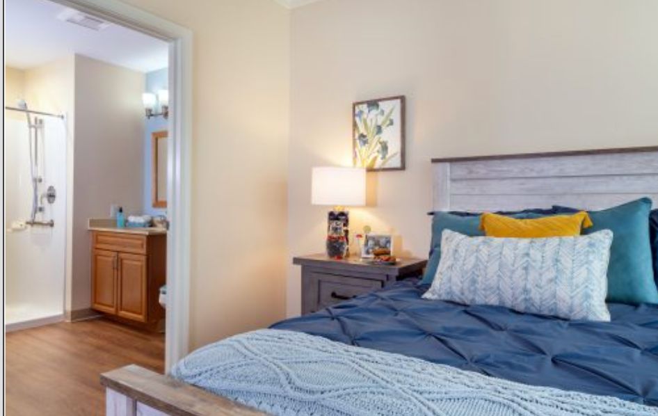 A cozy bedroom with a neatly made bed, bedside lamp, and wall art.