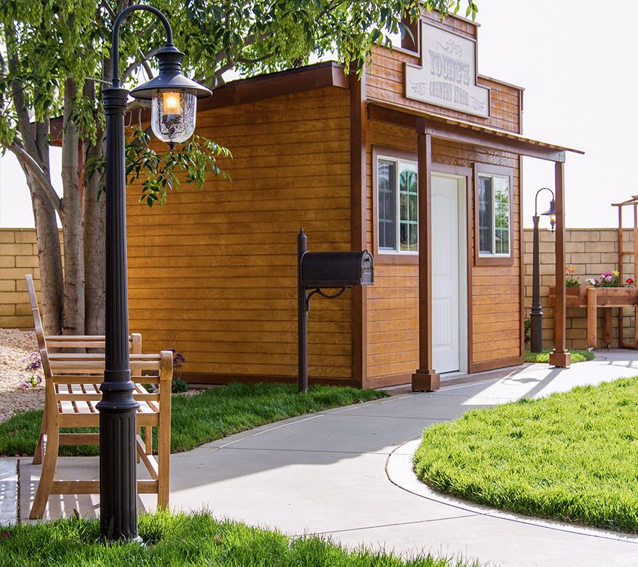 A cozy wooden shed in a well-maintained garden with a lamp post and outdoor seating.