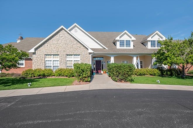 A suburban house with a stone facade, surrounded by well-maintained landscaping under a clear blue sky.