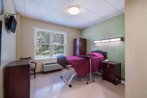 A well-lit patient room featuring a bed, chair, and storage, designed for comfort and care.