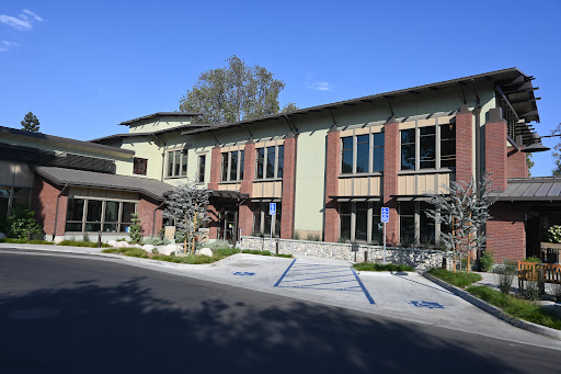 A modern architectural building with a blend of brick and green elements, featuring large windows and a welcoming entrance.