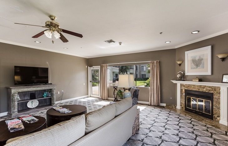 A spacious and well-lit living room with modern furnishings, including a large sofa, fireplace, television, and ceiling fan.
