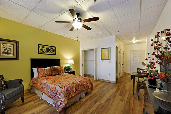 A cozy bedroom with warm-colored decor, featuring a ceiling fan and wooden flooring.