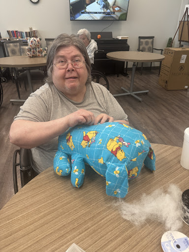 An elderly woman working on a colorful stuffed animal project at a crafting table.