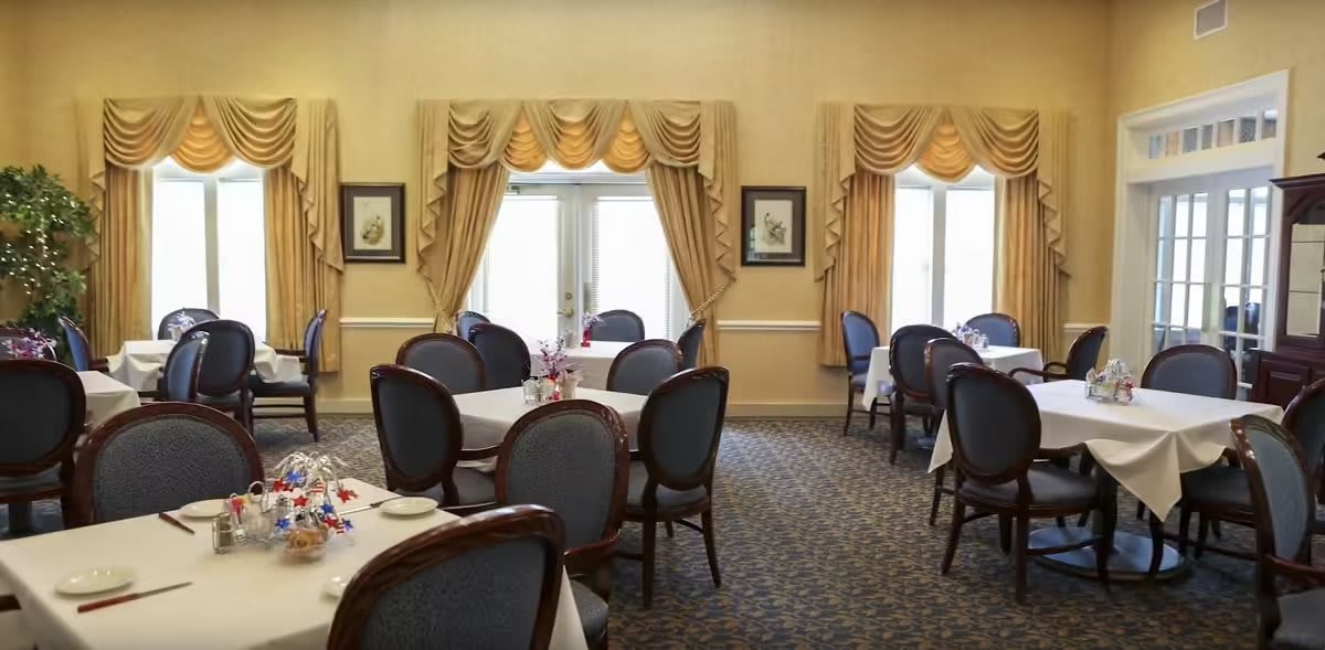 A formal dining room with elegantly set tables and chairs, featuring decorative curtains.