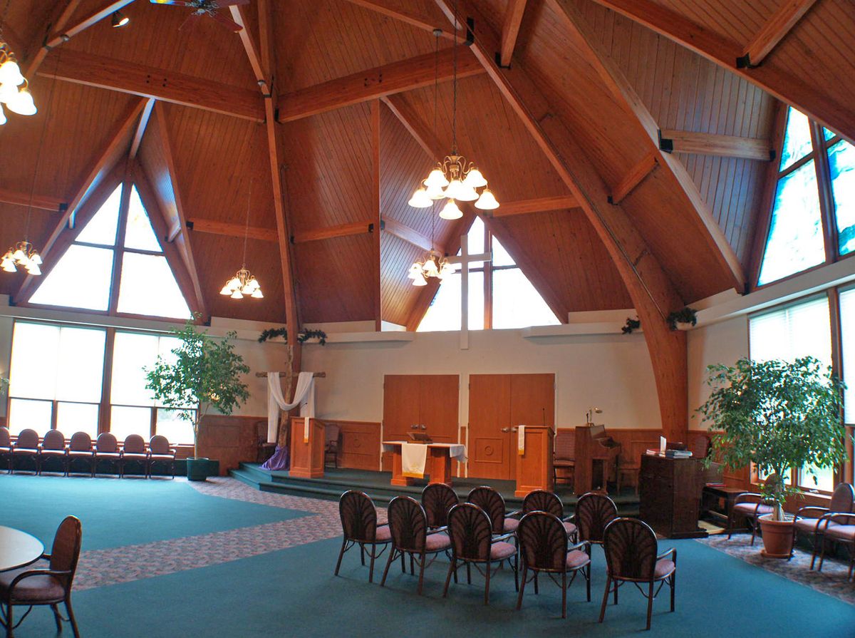Interior view of a modern church with wooden beams and large windows.