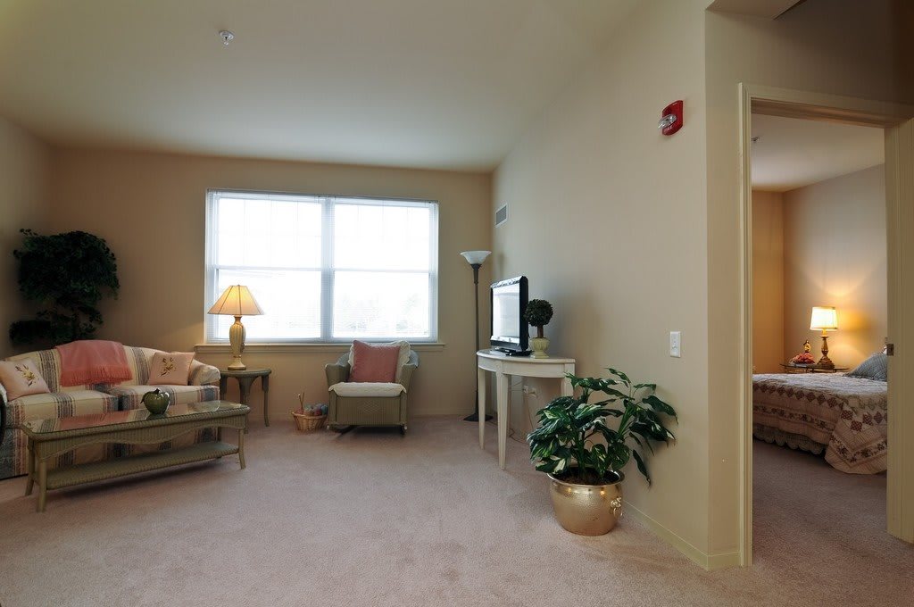 A cozy living room with a large window, comfortable seating, a lamp, and a television.