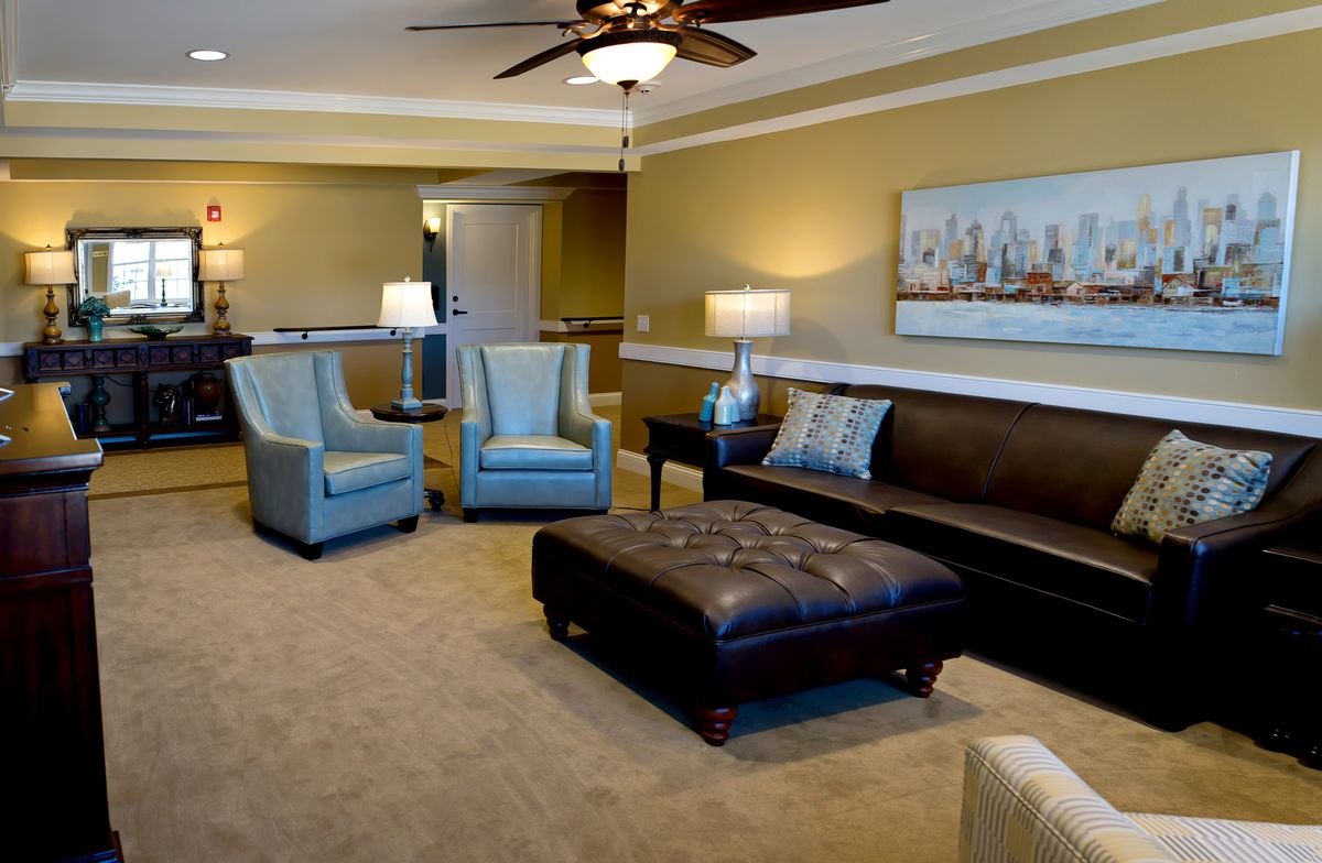 A well-furnished living room featuring a leather sofa, two armchairs, a large ottoman coffee table, and elegant lighting.