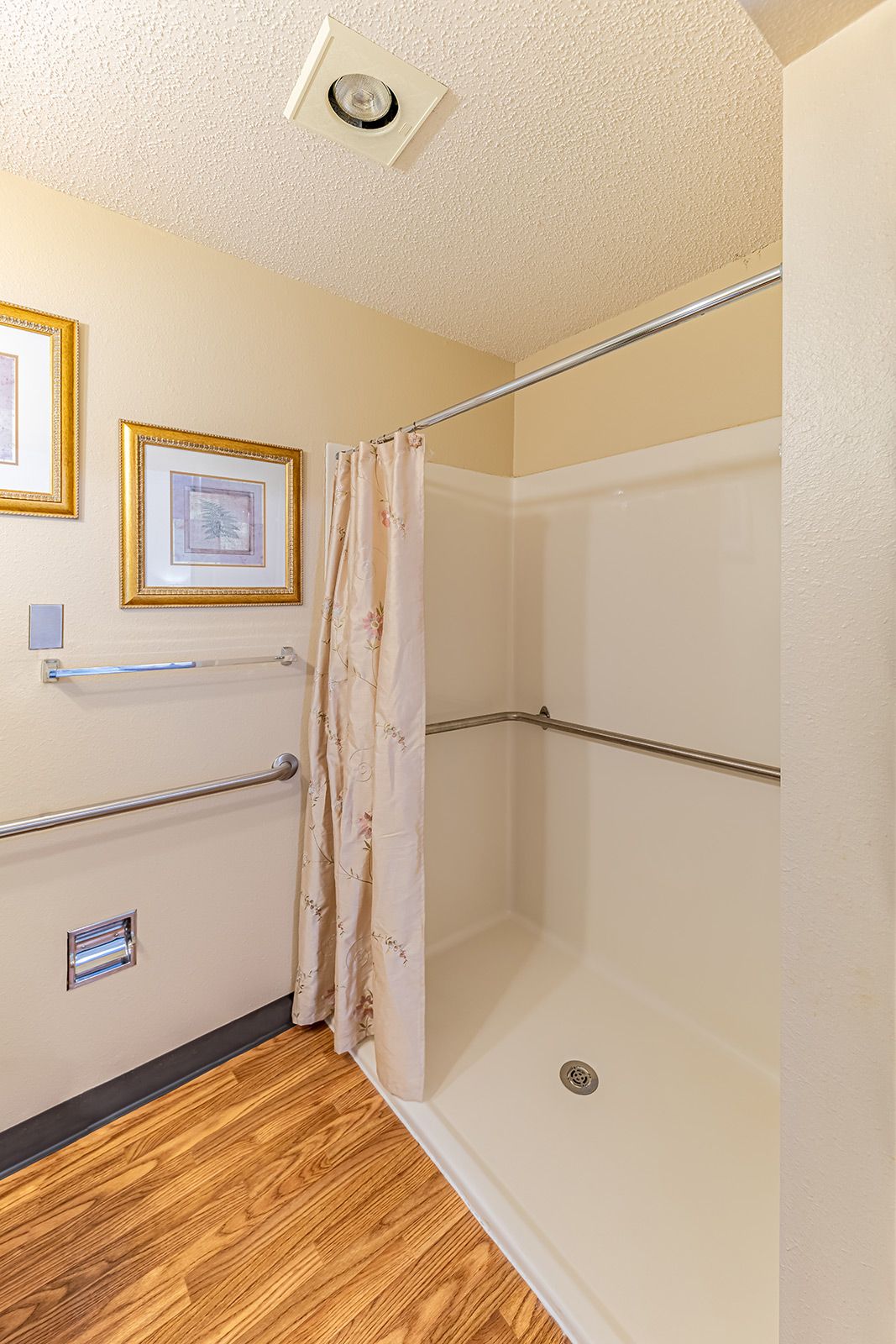 A bathroom featuring a shower with curtains, handrails, and framed artwork on the wall.