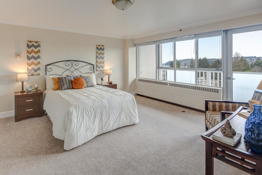A spacious and bright bedroom with a large bed, decorative pillows, and expansive windows offering a serene view.