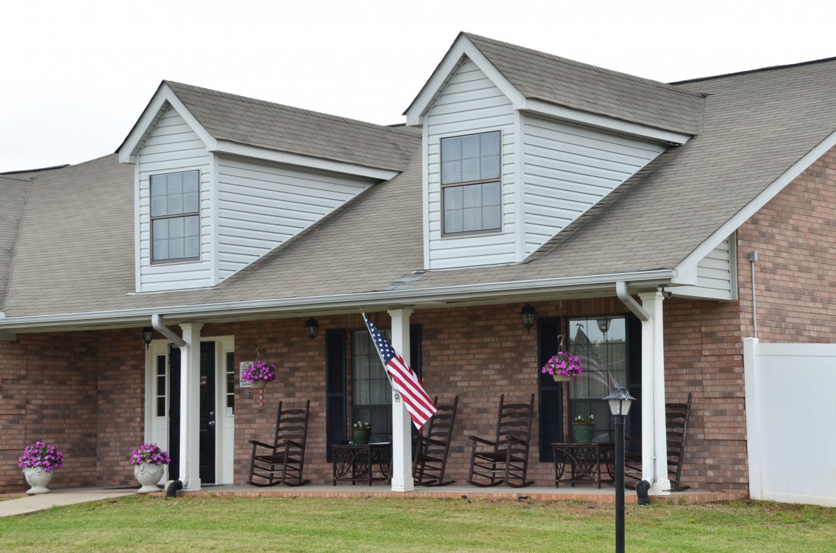 A suburban house with a front porch, displaying an American flag and several rocking chairs.