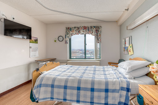 A well-lit hospital room featuring a bed with a checkered blanket and a window offering a view.