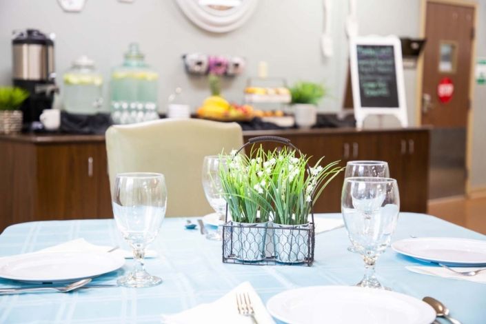 A dining table set with glasses and a green plant centerpiece, ready for a casual indoor gathering.